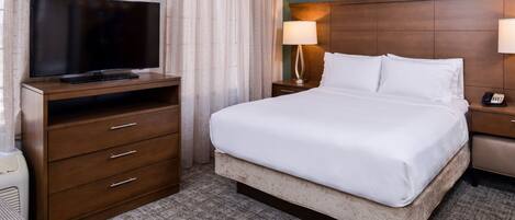 A hotel room with a bed, a television on a wooden dresser, a lamp, and a telephone on the nightstand.