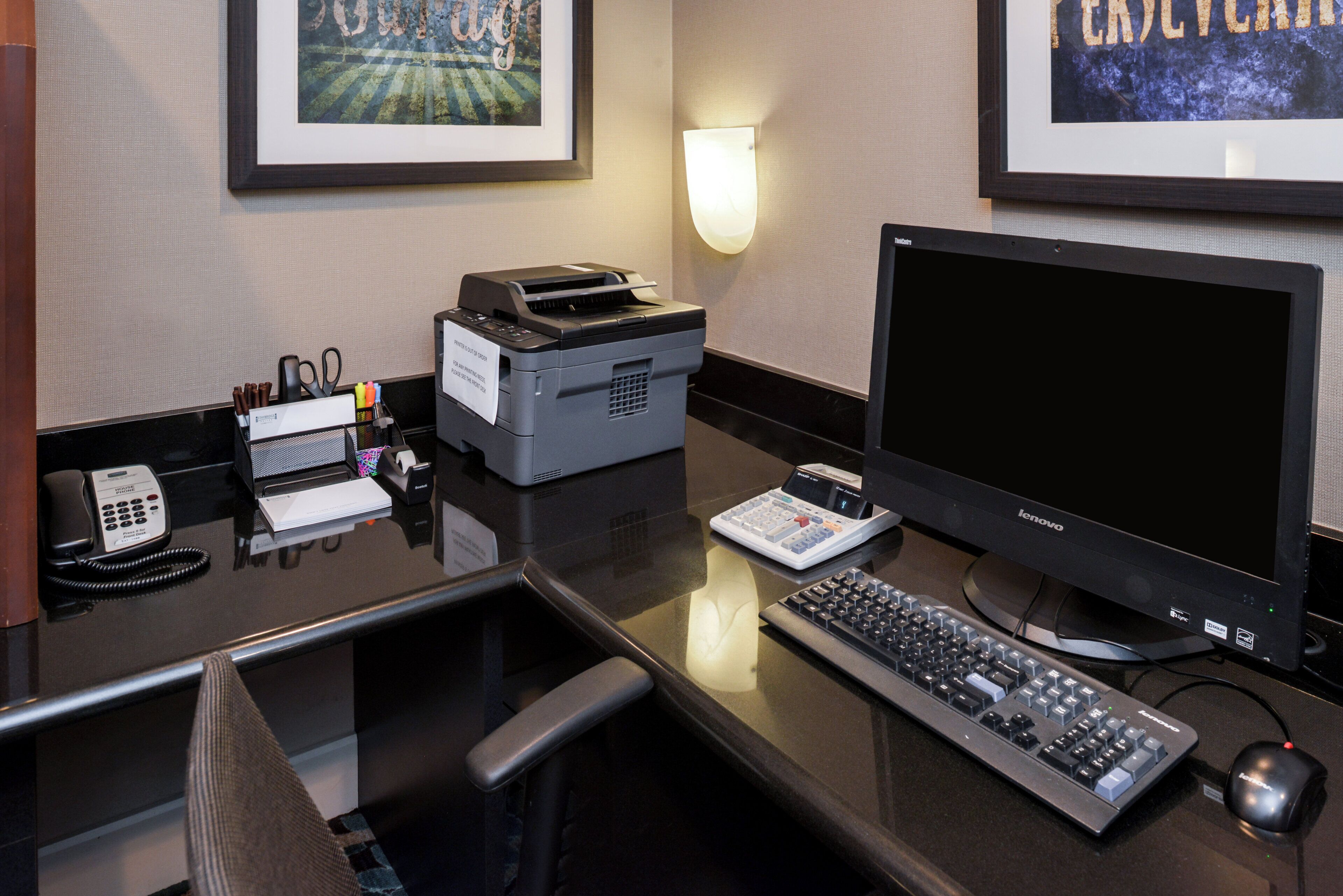 A hotel reception desk with a desktop computer, a printer, a telephone, and a keyboard.
