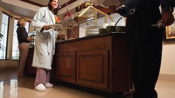 A hotel lobby with a reception desk, a person in a robe, and another person holding a plate.