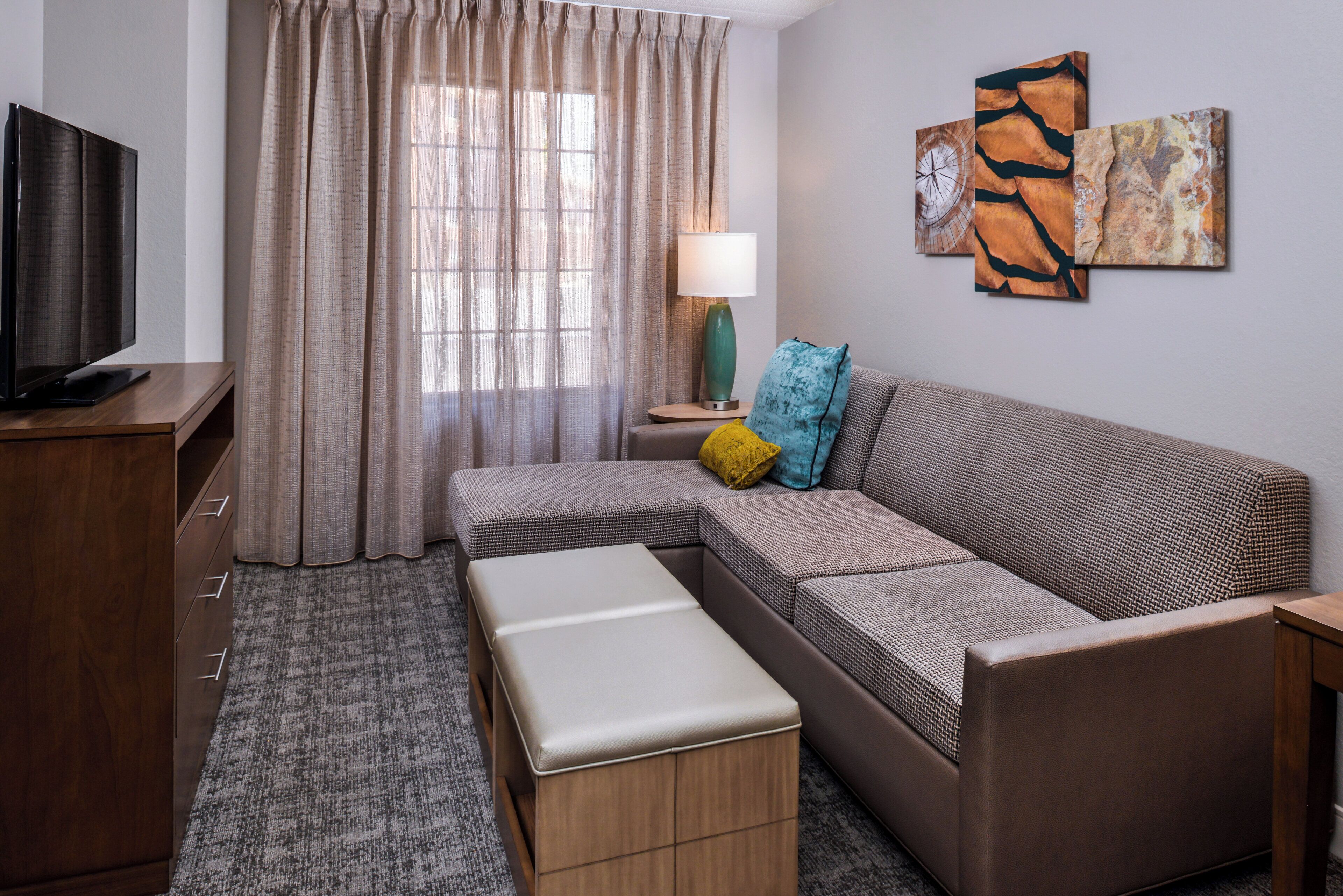 A modern living room with a sofa, a TV, a lamp, and artwork on the wall.