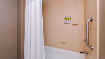 A bathroom with a bathtub, a shower curtain, a handrail, and toiletries on the wall.