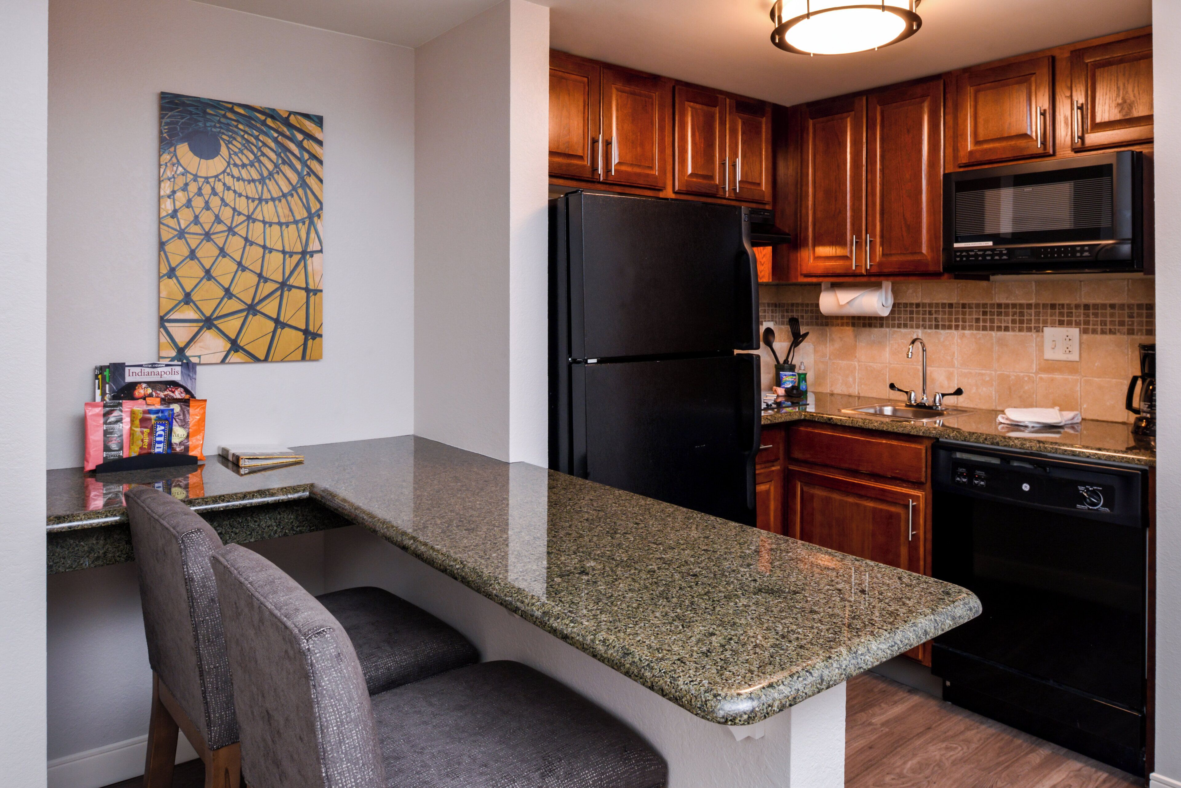 A kitchen with a granite countertop, wooden cabinets, a black refrigerator, a microwave, and a dishwasher.