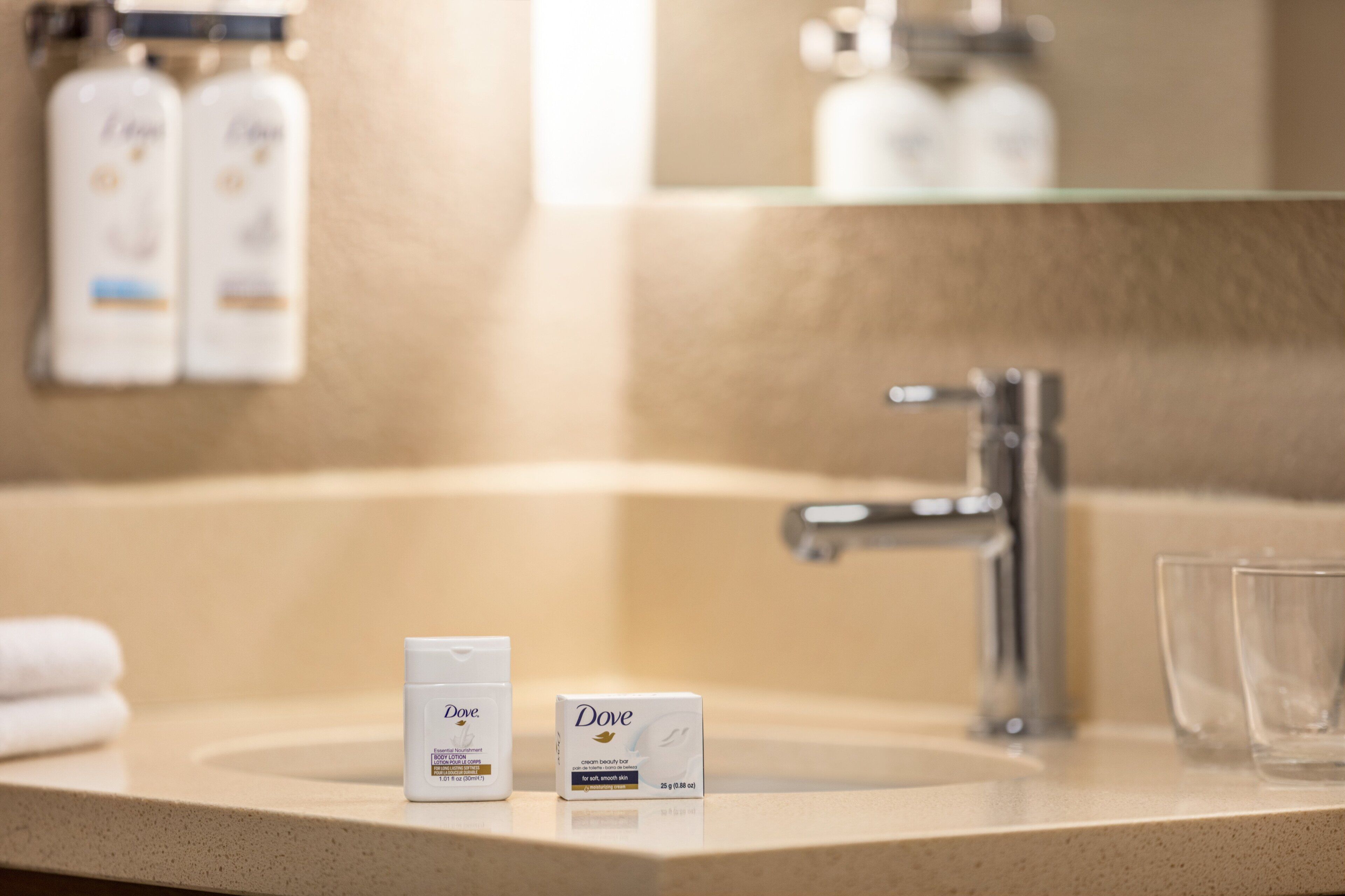A bathroom sink with Dove skincare products, a mirror, and a glass.