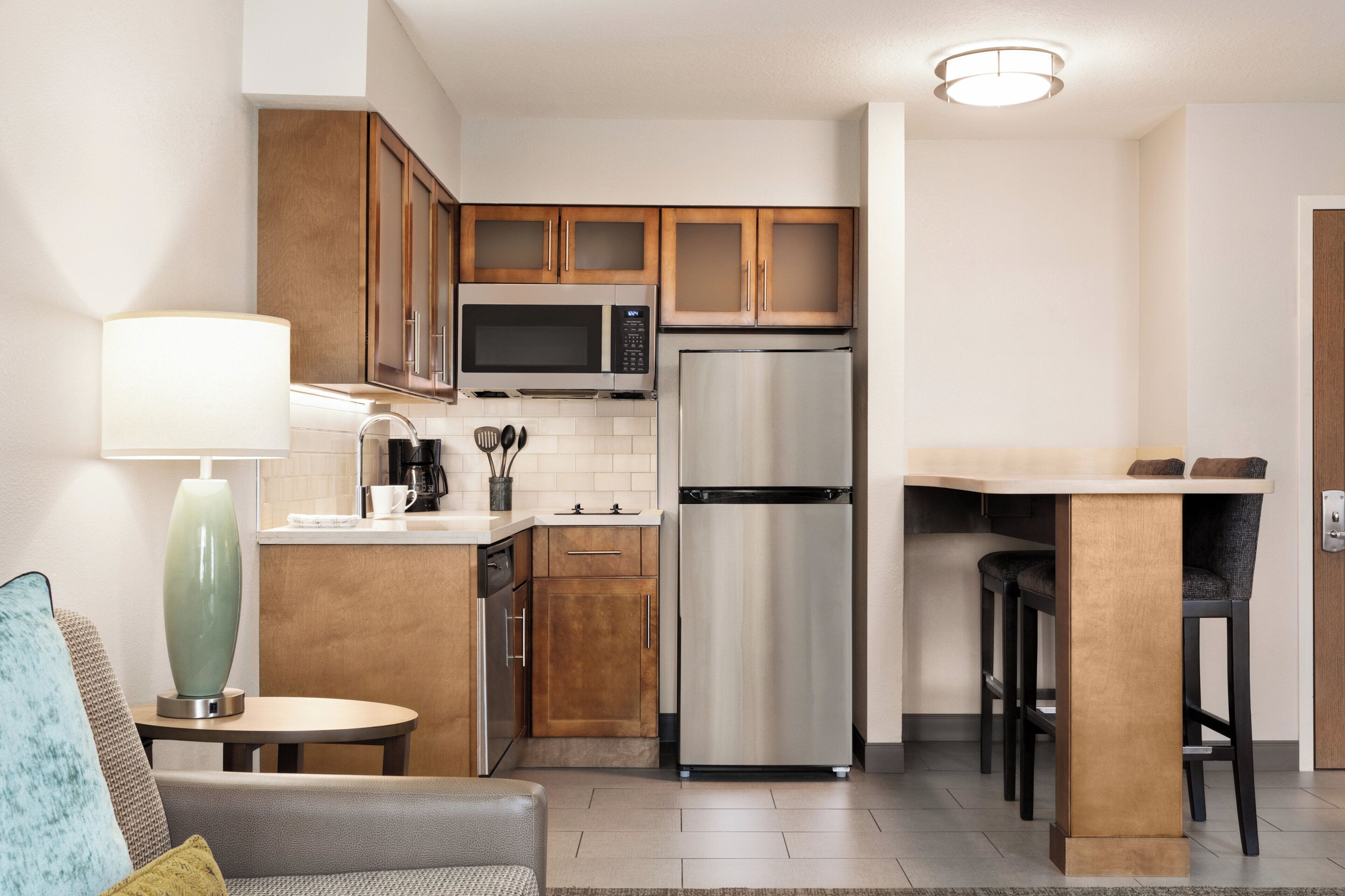 A compact kitchen with wooden cabinets, a stainless steel refrigerator, a microwave, and a coffee maker.