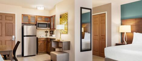 A hotel room with a kitchenette, a bed, a desk, and a chair.