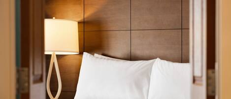A hotel room with a wooden headboard, a white bed, and a bedside lamp.