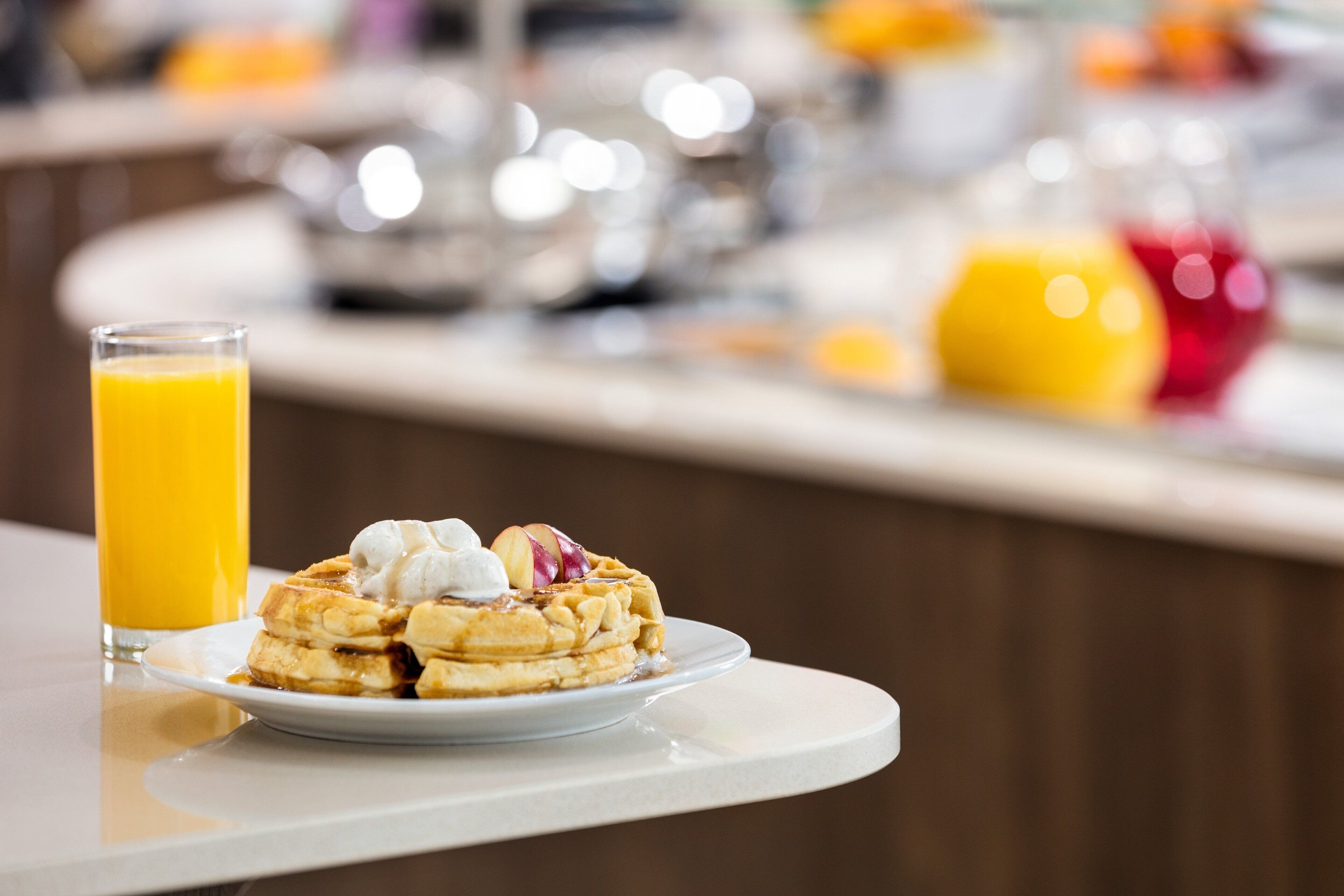 A breakfast plate with pancakes, a glass of orange juice, and a bowl of fruit on a table.