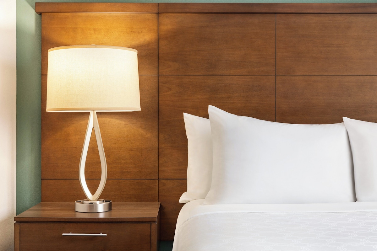A neatly made bed with white linens and a wooden nightstand beside it.