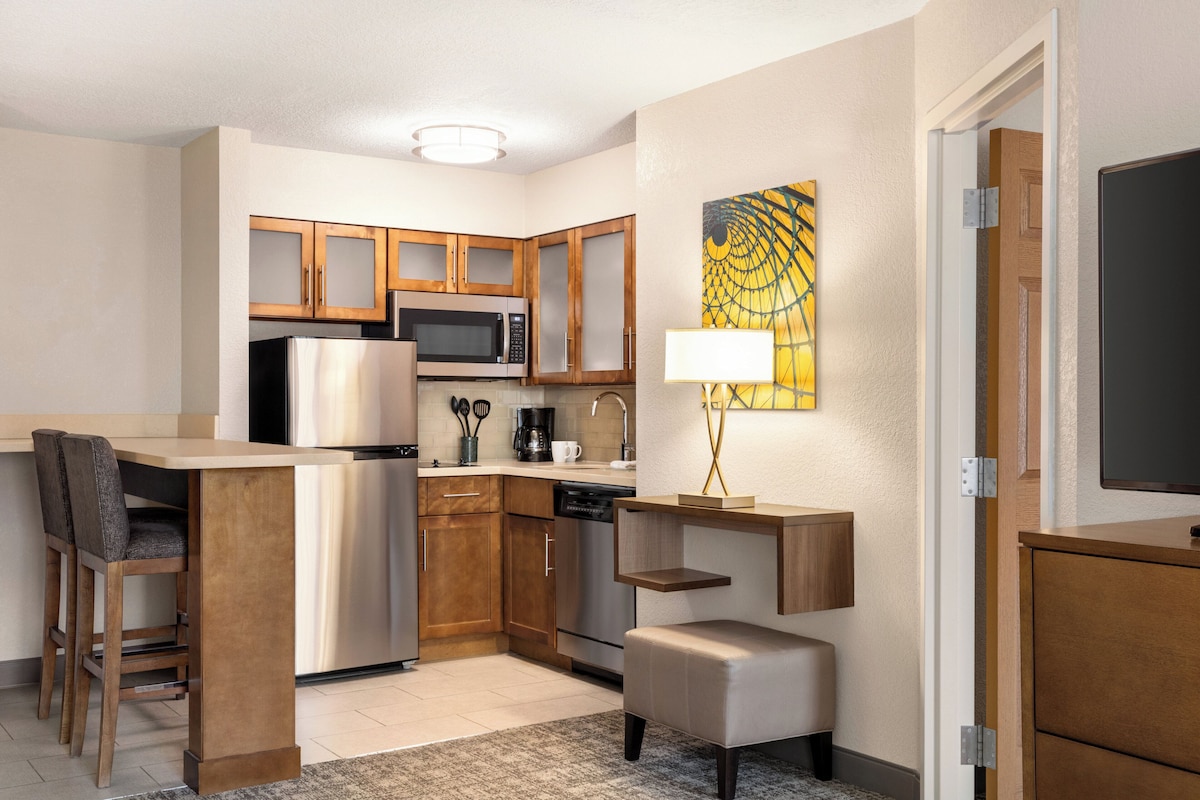 A compact kitchen with a microwave, refrigerator, and coffee maker. There is a small dining area with a bench and chairs.