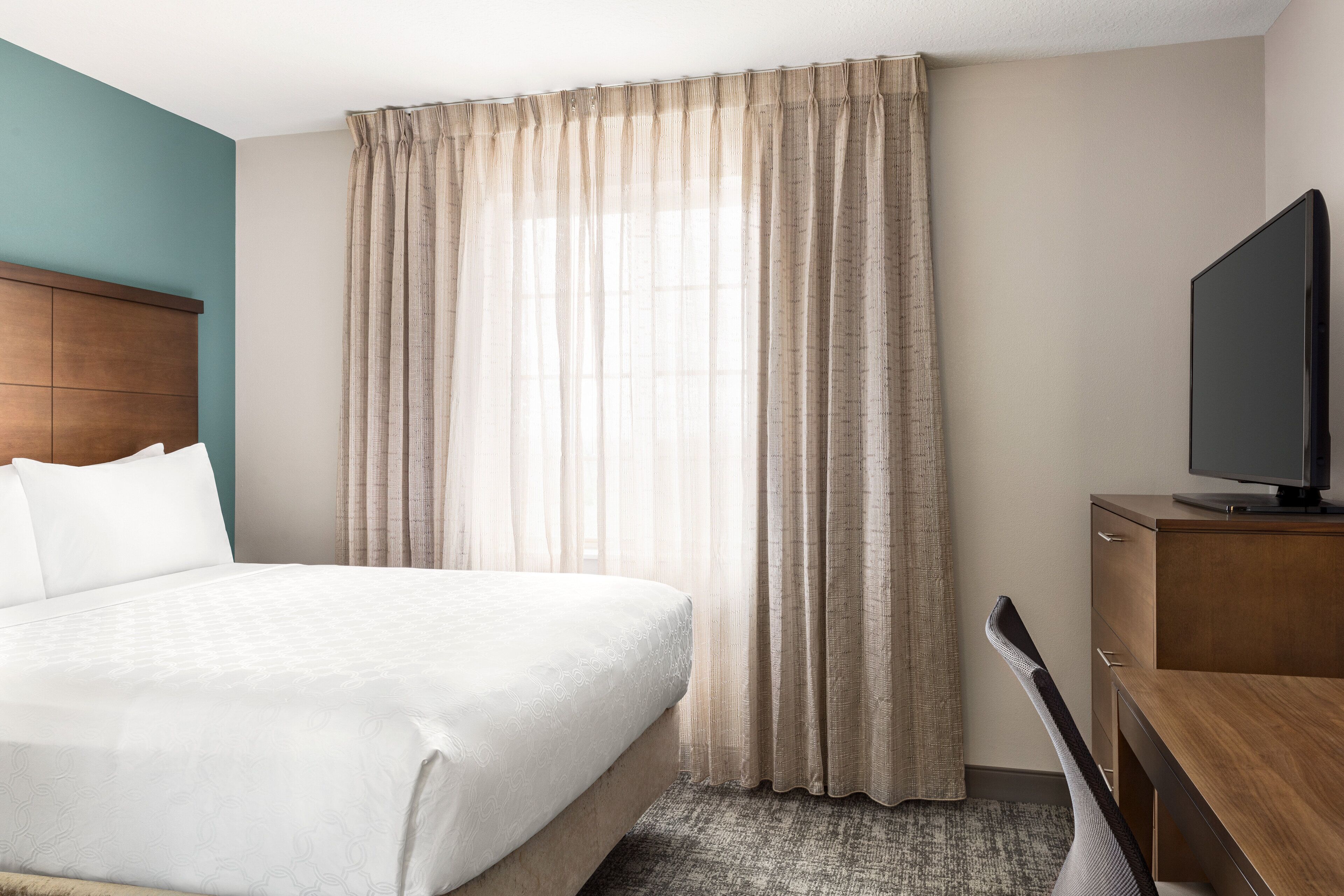Une chambre d’hôtel avec un lit, un bureau, une télévision et une fenêtre avec des rideaux.