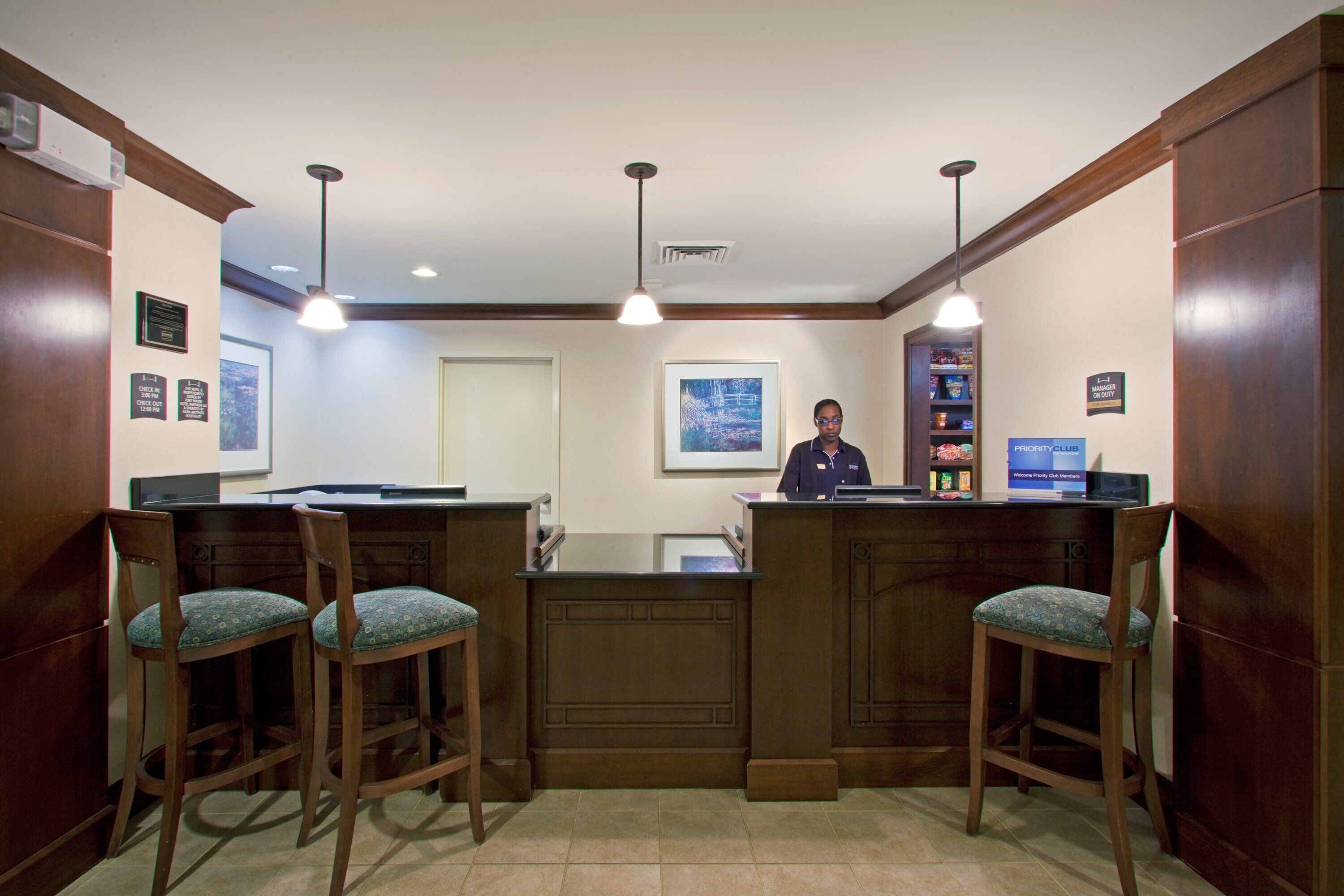 A reception area with a wooden counter, two bar stools, a receptionist, and a framed picture on the wall.