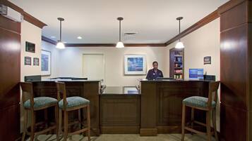 A reception area with a wooden counter, two bar stools, a receptionist, and a framed picture on the wall.