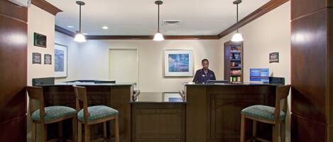 A reception area with a wooden counter, two bar stools, a receptionist, and a framed picture on the wall.