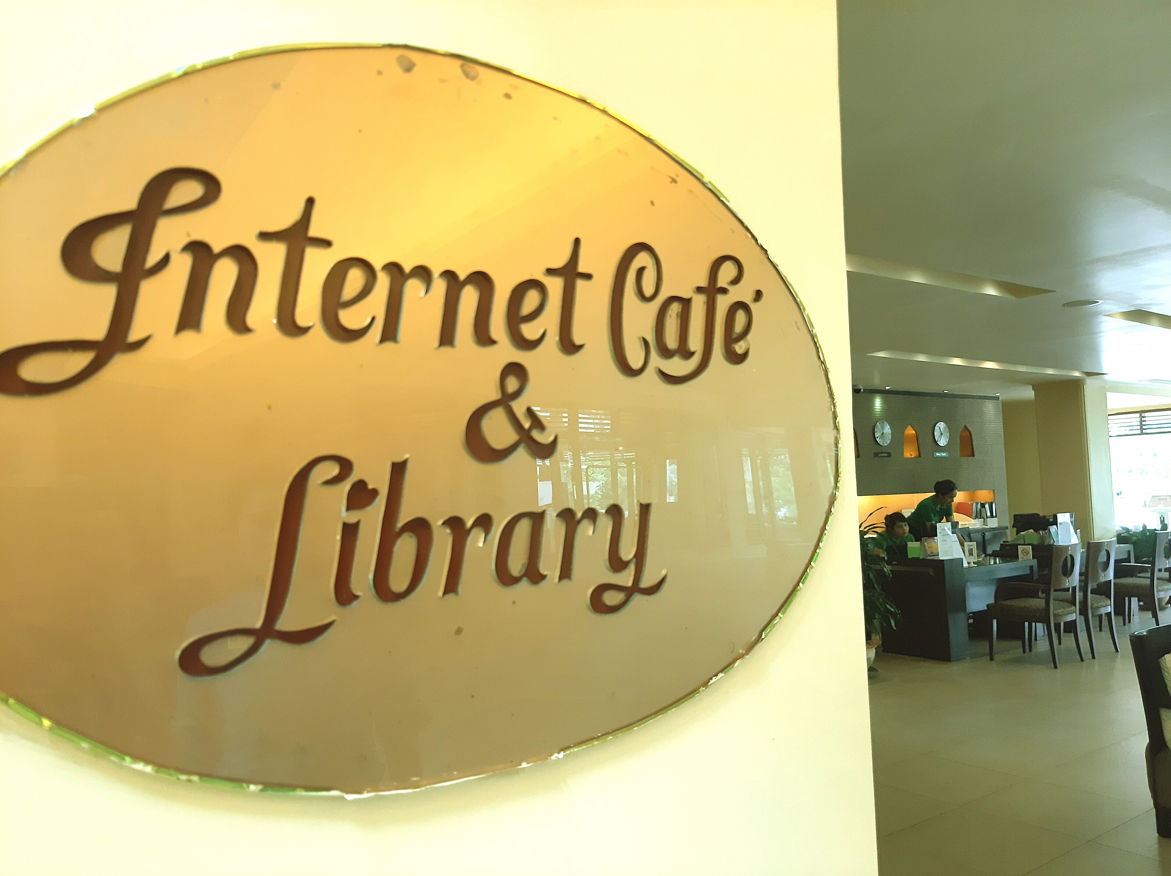Señalización de 'Internet Cafe & Library' con un interior moderno que incluye asientos y una barra de atención.