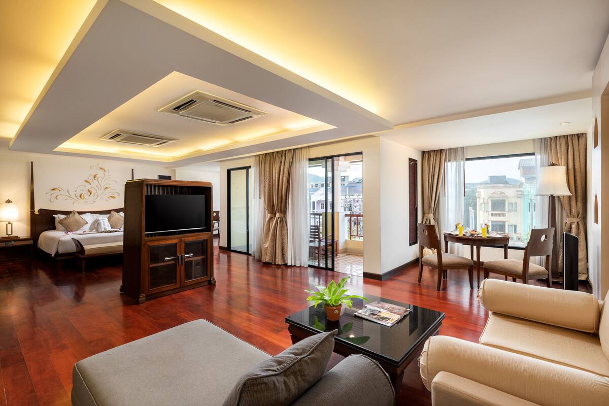 A modern hotel room with a bed, sofa, TV, and dining area.
