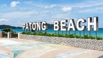 A sign reading "PATONG BEACH" with a view of the ocean and a stone wall.