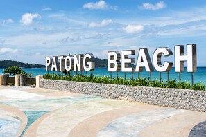 Ein Schild mit der Aufschrift 'PATONG BEACH', mit Blick auf den Ozean und einer Steinmauer.
