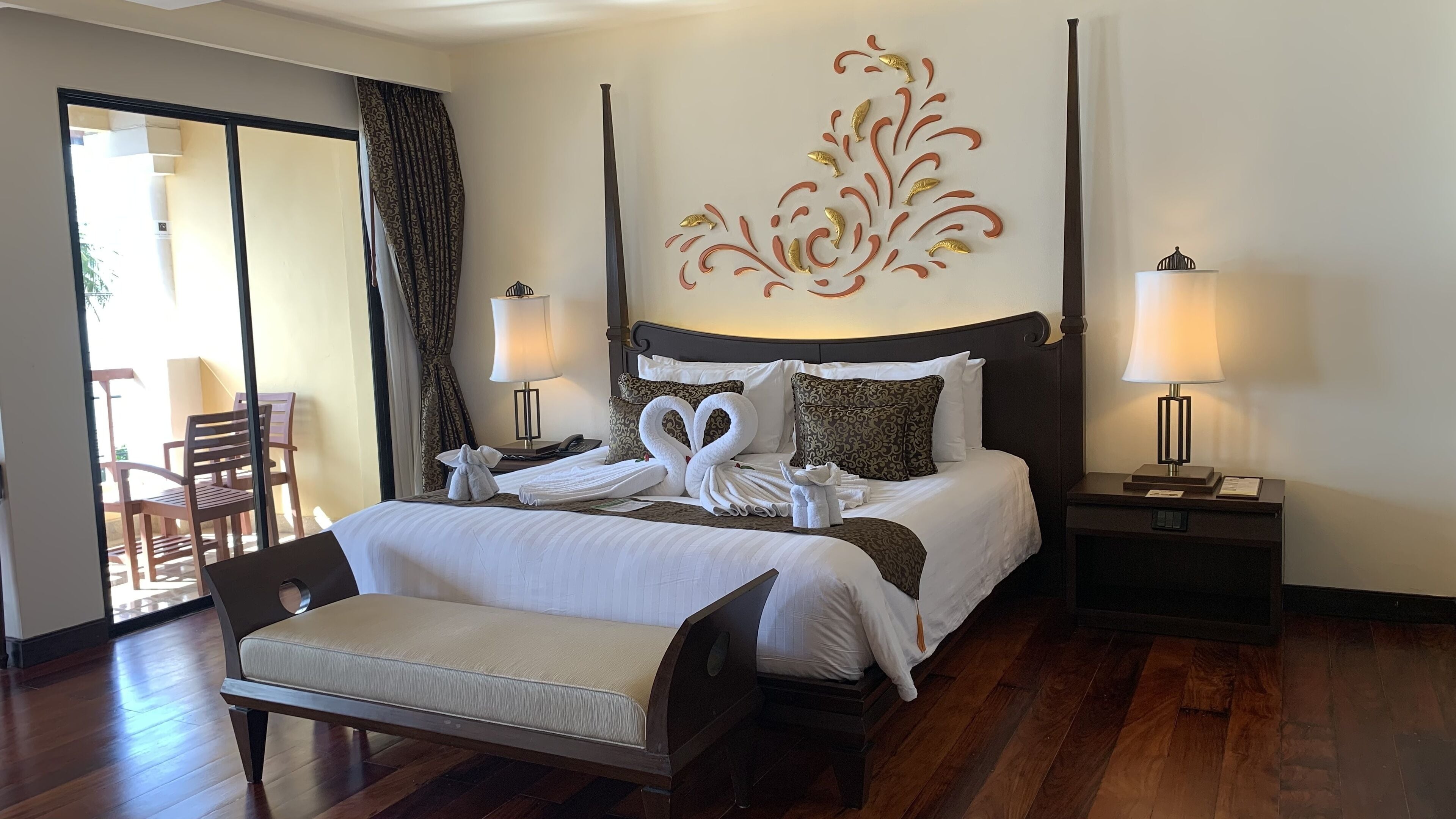 A hotel room with a large bed, two bedside tables, a chair, a decorative wall piece, and a view of the outside.