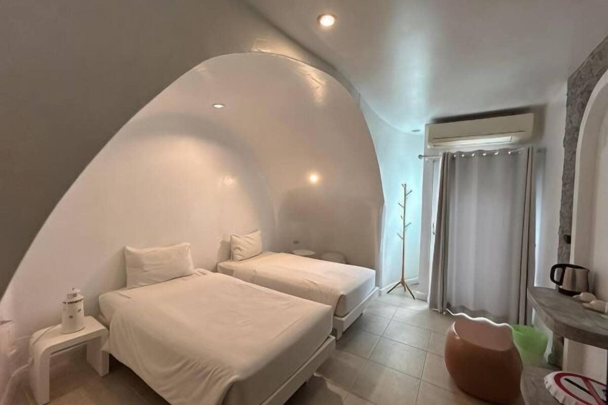 A bedroom with two beds, a curved ceiling, a small table, and a chair.