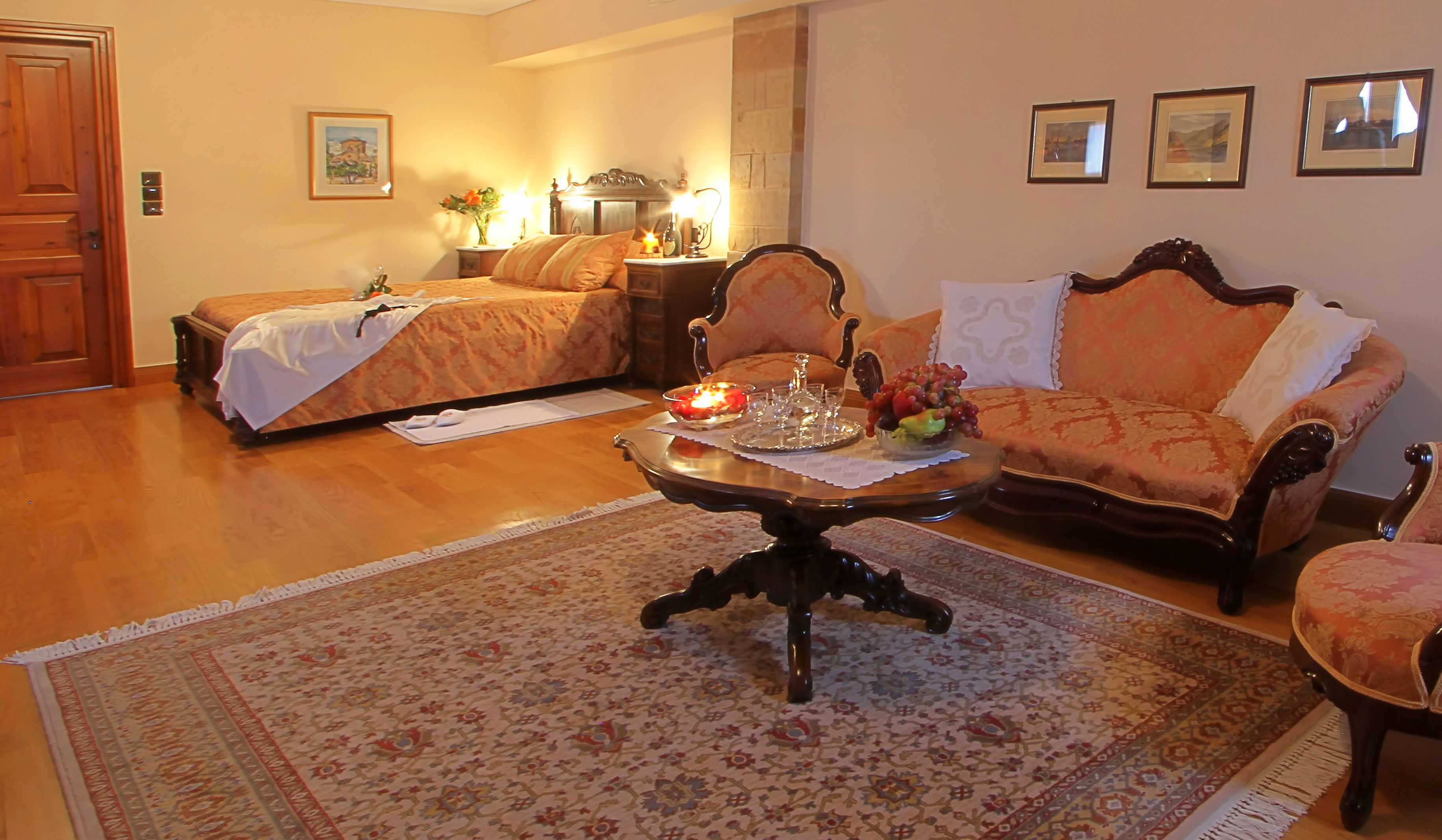 A hotel room with a bed, a sofa, a coffee table with decorative items, a rug, and framed pictures on the wall.