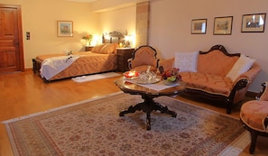 A hotel room with a bed, a sofa, a coffee table with decorative items, a rug, and framed pictures on the wall. - Argentikon Luxury Suites (Chios)