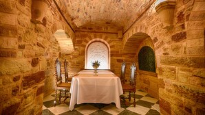 Habitació de parets de pedra, amb un terra estampat, una taula amb estovell blanc i dues cadires ornamentades.