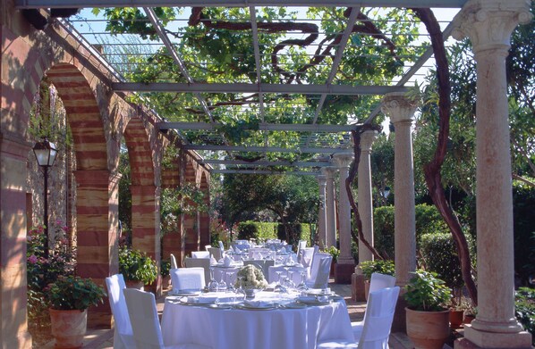 An outdoor dining area with white tables and chairs, surrounded by columns and arches, under a pergola. - Argentikon Luxury Suites (Chios)