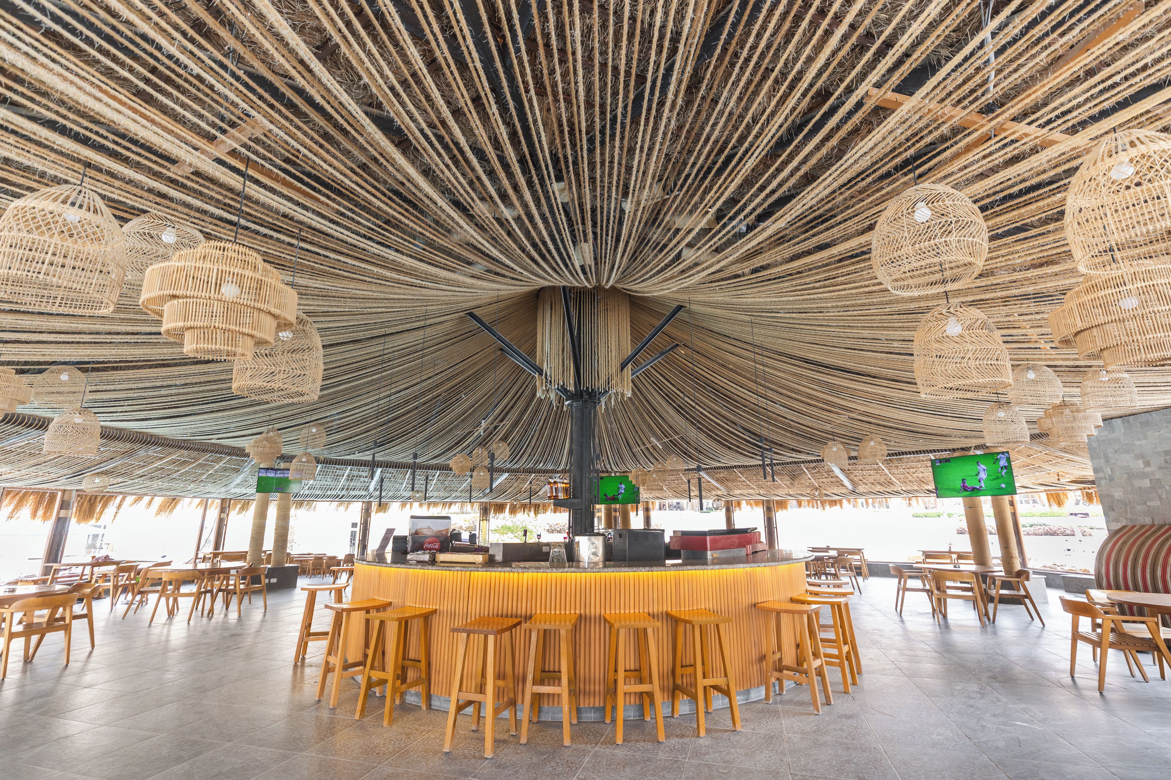 An open-air dining area with a central bar, wooden furniture, and a thatched ceiling.