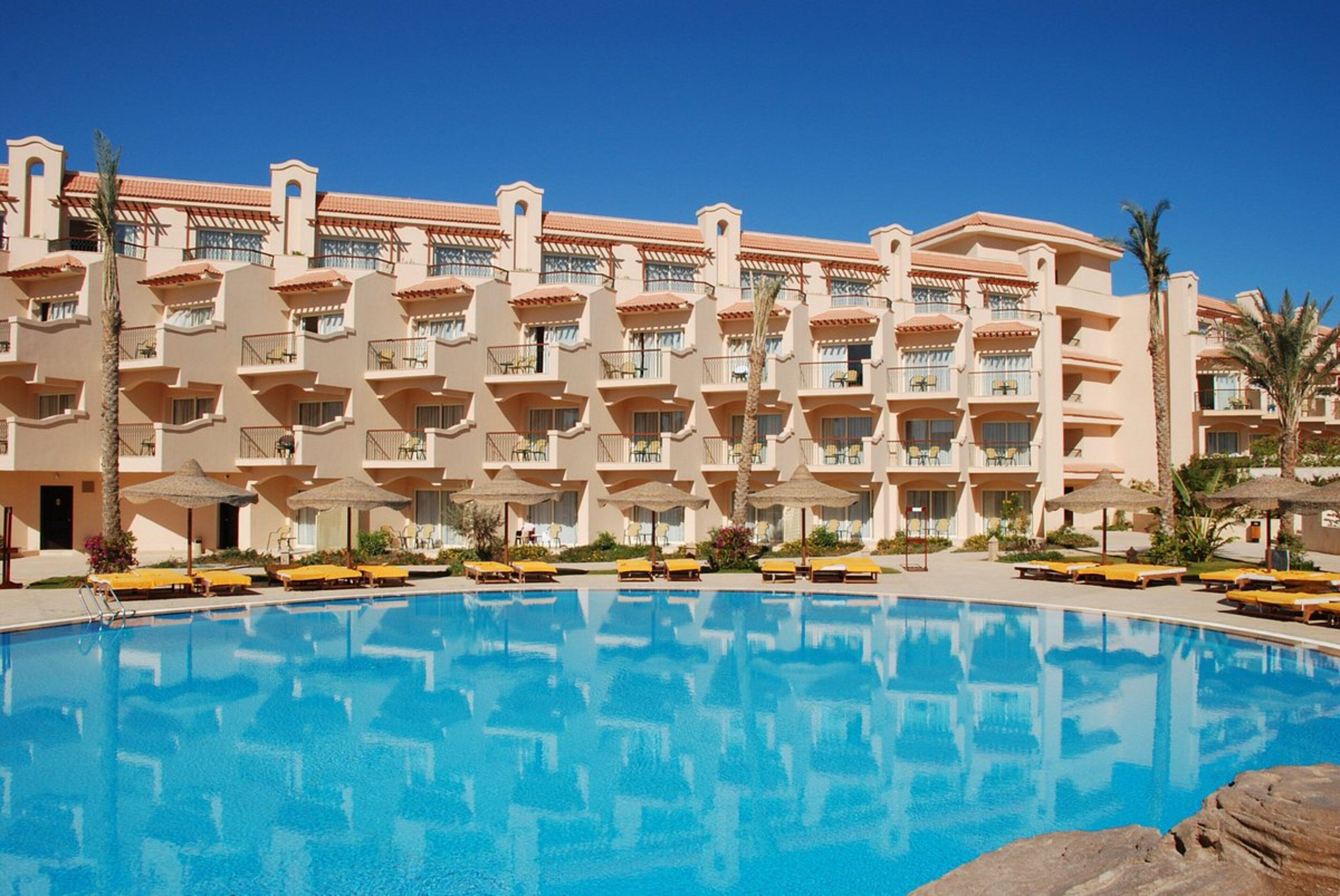 Un hotel con una piscina grande, varios balcones y tumbonas.