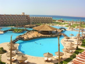 Un resort con diverse piscine, lettini prendisole e costruzioni a tetto di paglia.