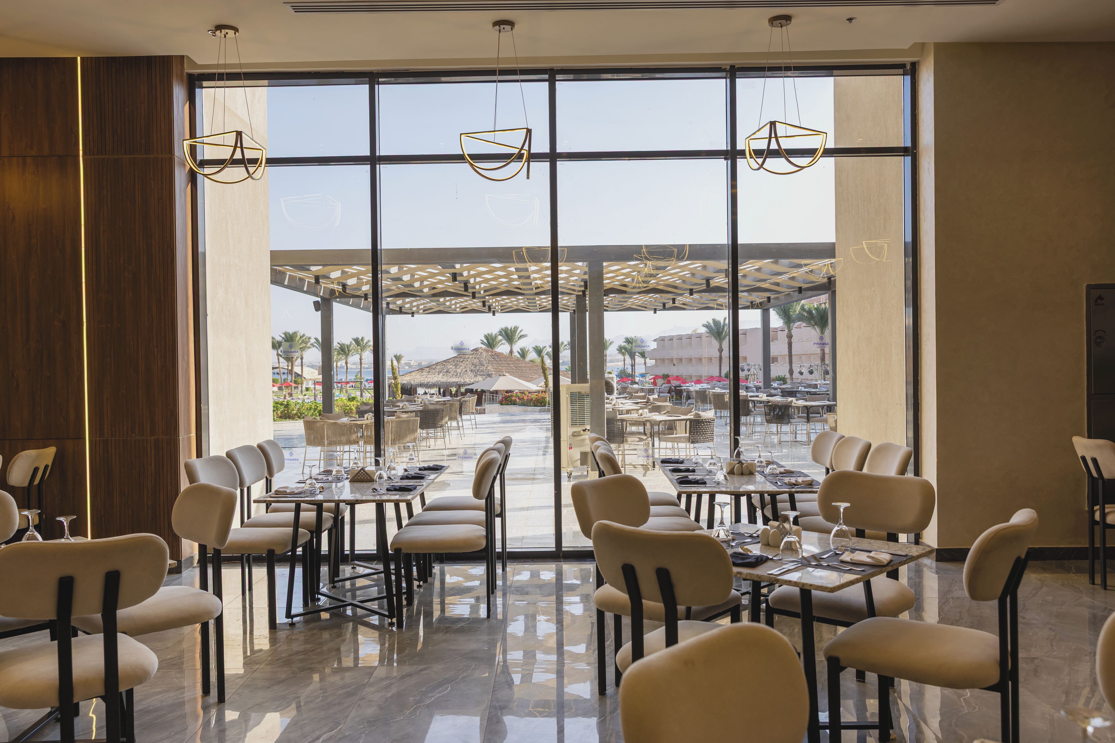 Un restaurante con vistas a un área de estar al aire libre, mesas, sillas y una decoración interior moderna.