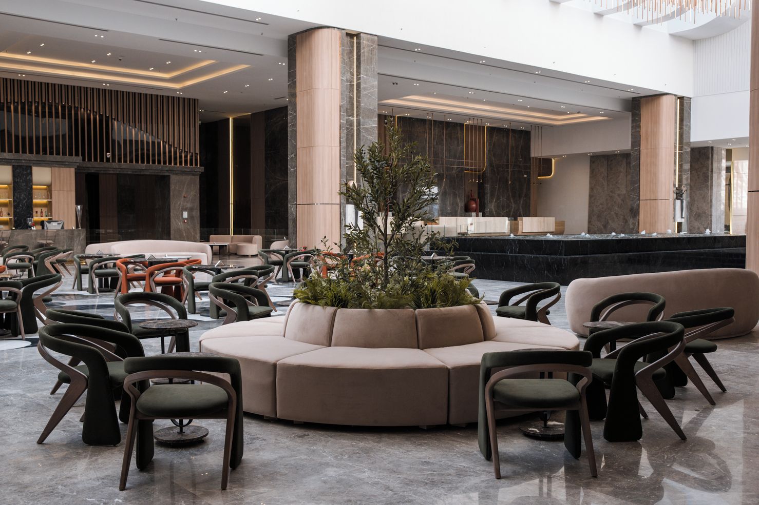 Un vestíbulo moderno con una zona de estar central, un mostrador de recepción y una planta grande.