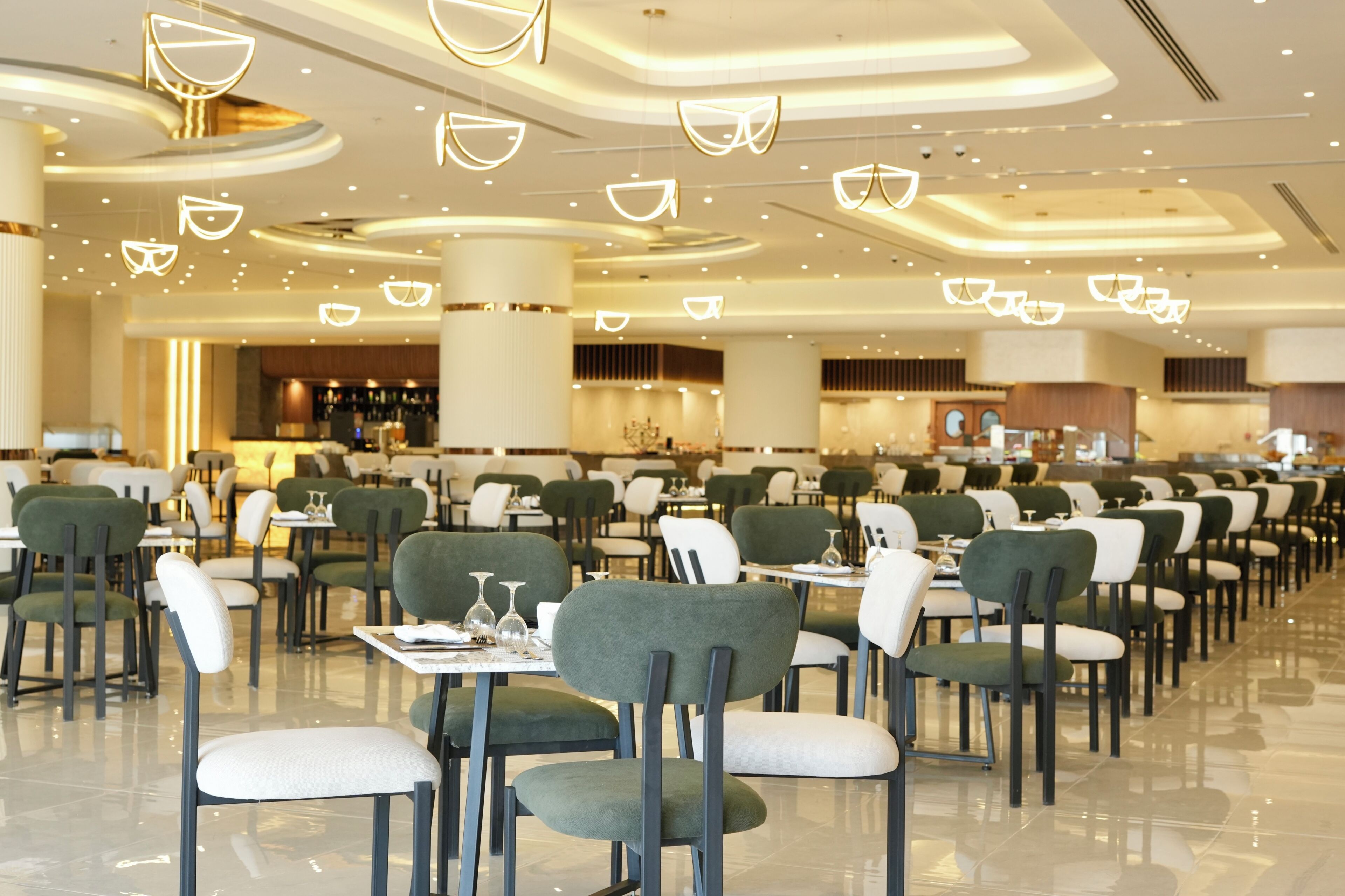 A spacious dining area with multiple tables and chairs, a bar in the background, and modern ceiling lighting.