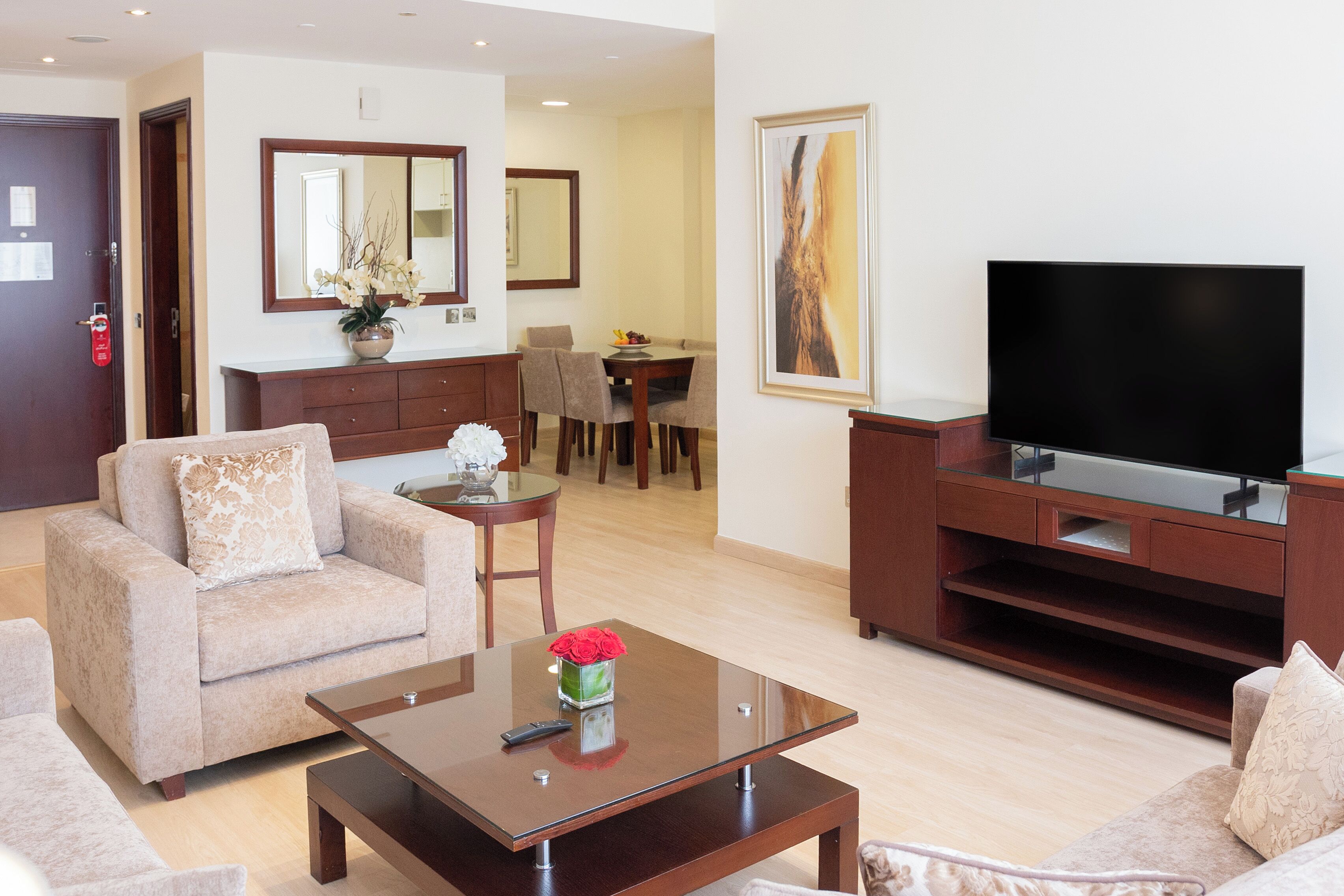 Un soggiorno moderno con un divano, un tavolino da caffè con un vaso di fiori, una TV su un mobile in legno e un'area pranzo sullo sfondo.