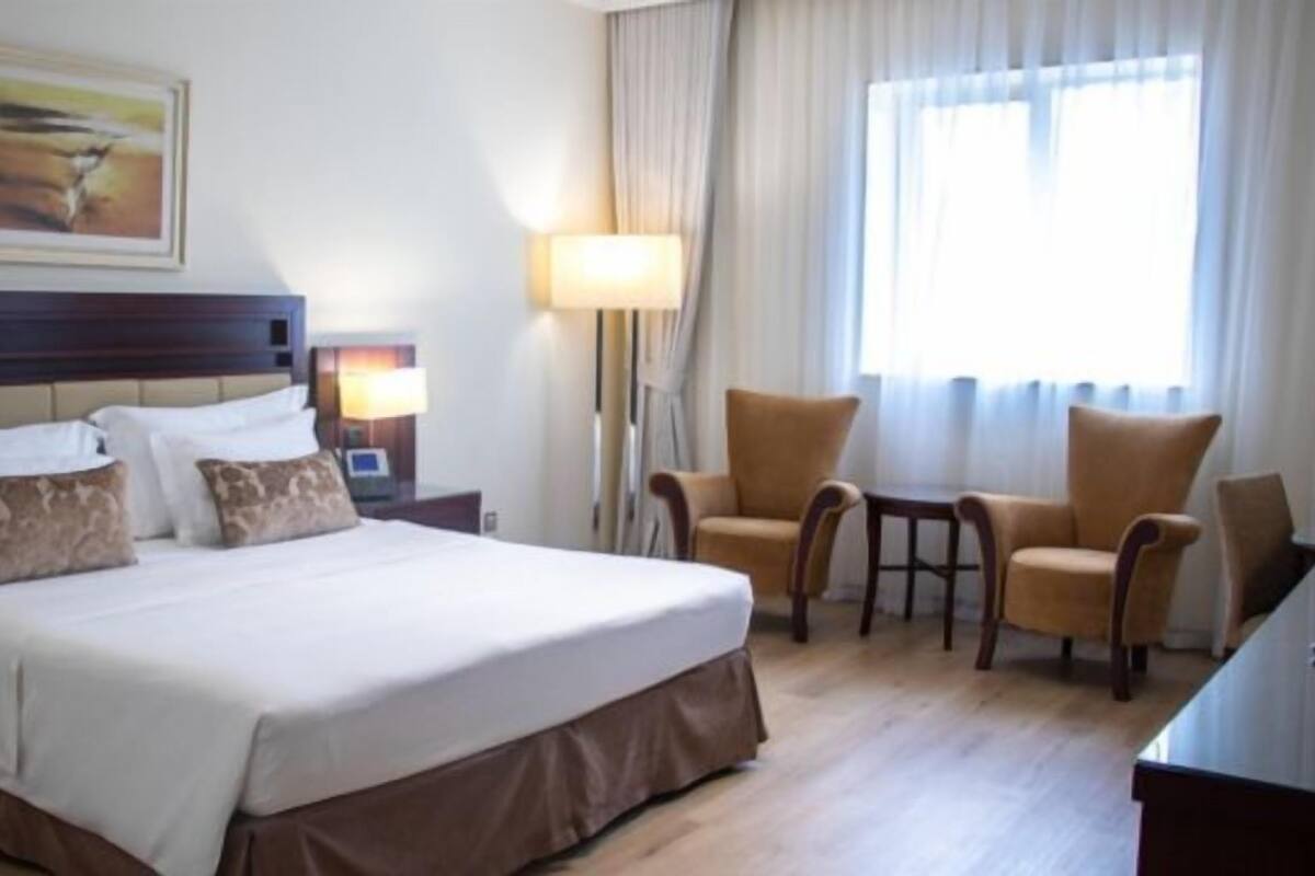 Hotellihuone, jossa on suuri sänky, kaksi yöpöytää, työpöytä, kaksi tuolia, lamppu ja taulu seinällä.