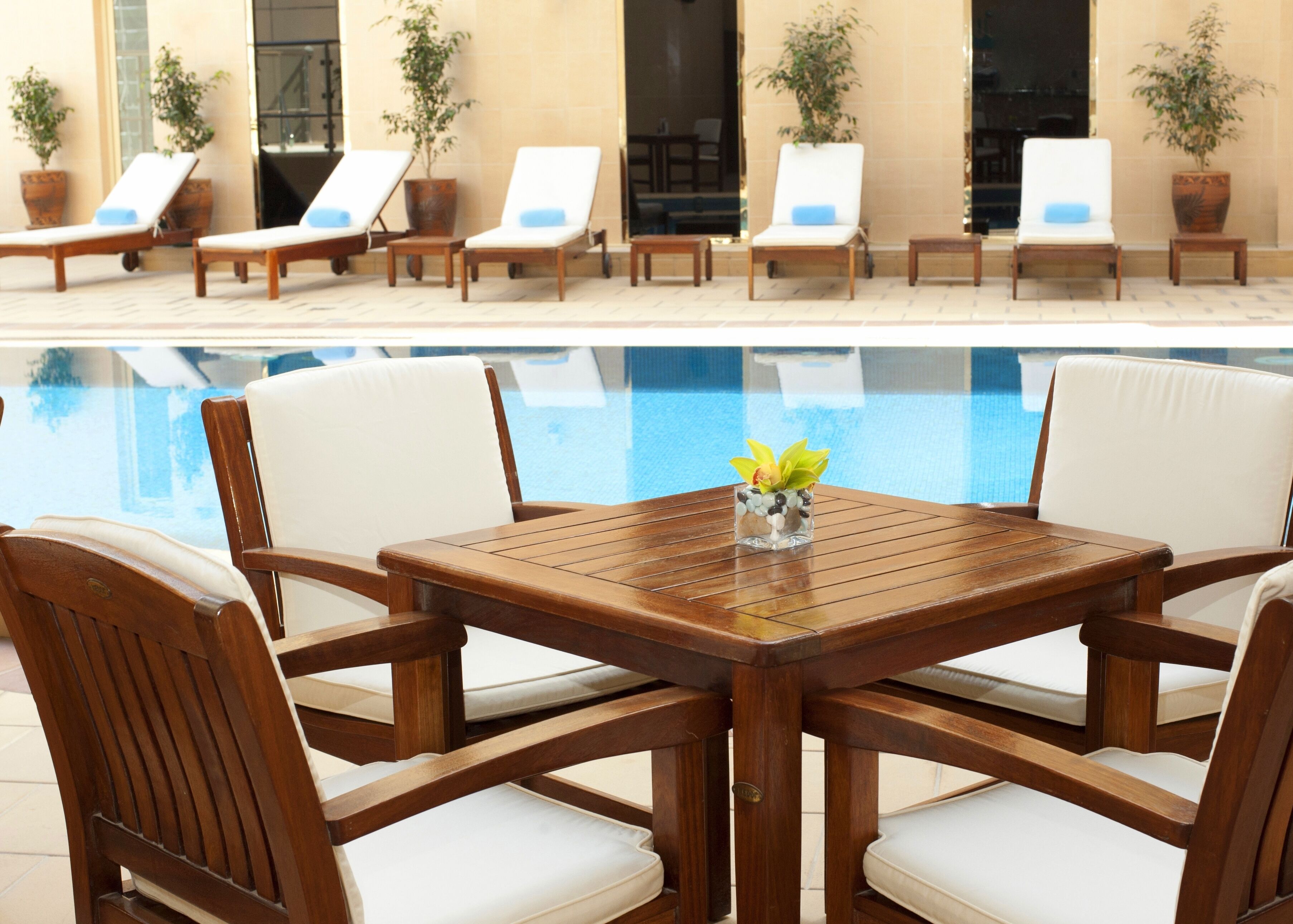 A poolside area with wooden lounge chairs and a table with a vase of flowers.