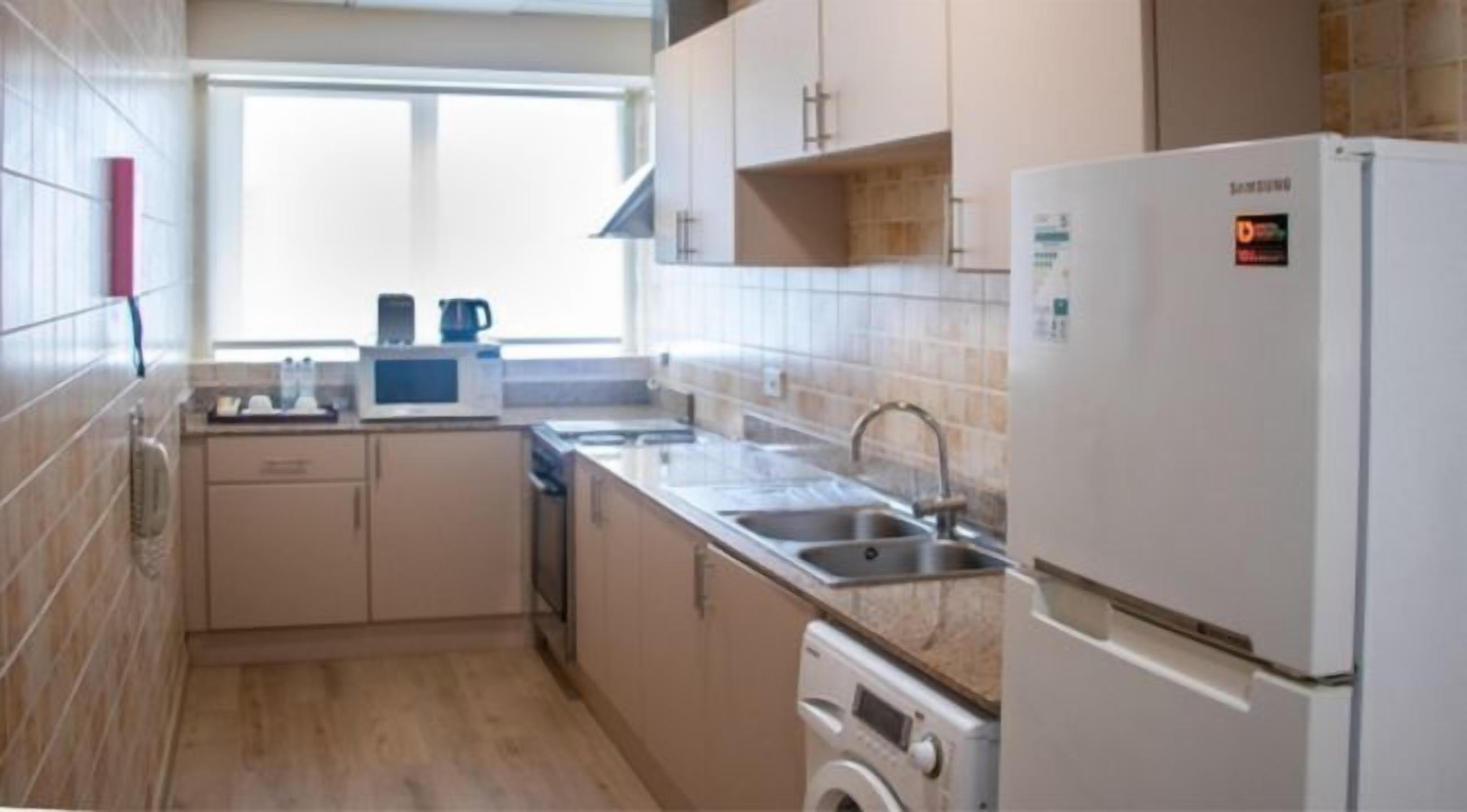 A compact kitchen with a microwave, kettle, sink, and washing machine.