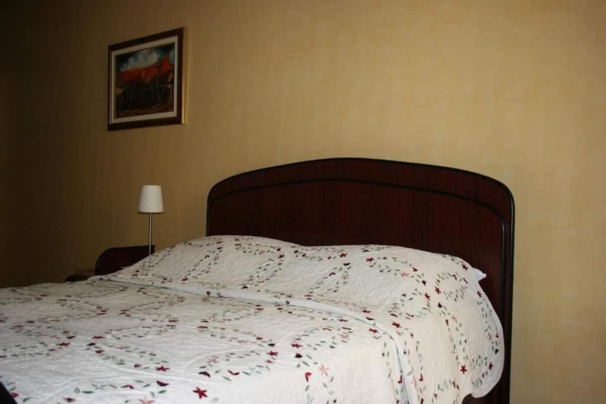 Un lit bien fait, recouvert d’une couvre-lit à motifs floraux, avec une tête de lit en bois et une seule lampe de chevet.