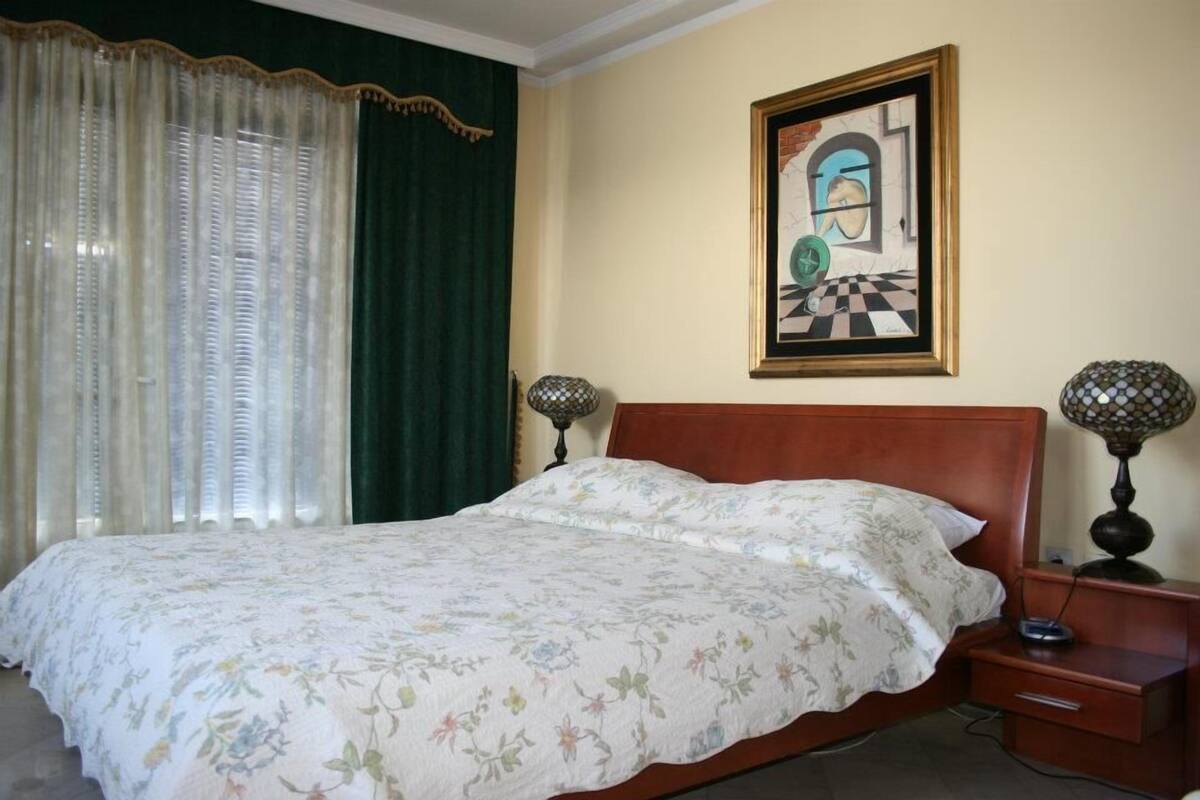 A neatly made bed with a floral bedspread, a framed artwork on the wall, and a lamp on a bedside table.