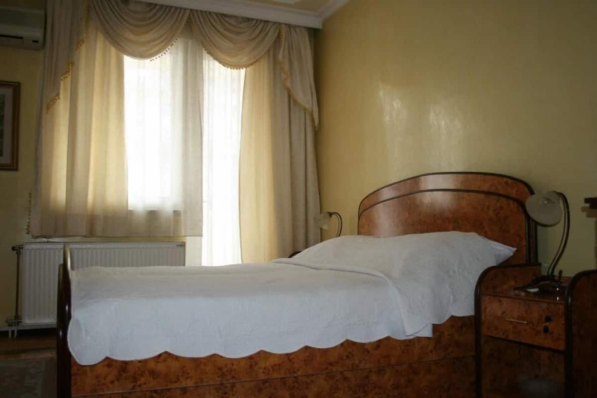 Un lit simple avec une tête de lit en bois, dans une pièce aux murs de couleur crème et avec un radiateur dans un coin.