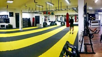 Academia com equipamentos de ginástica, saco de pancadas e área com tatame amarelo e preto.