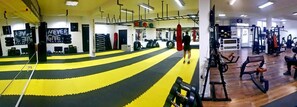 Un gimnasio con equipo de ejercicio, un saco de boxeo y una zona con colchonetas amarillas y negras.