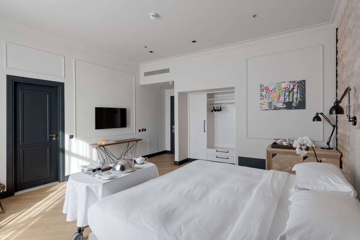 A hotel room with a large bed, a desk with a flat-screen TV, a wardrobe, and a painting on the wall.