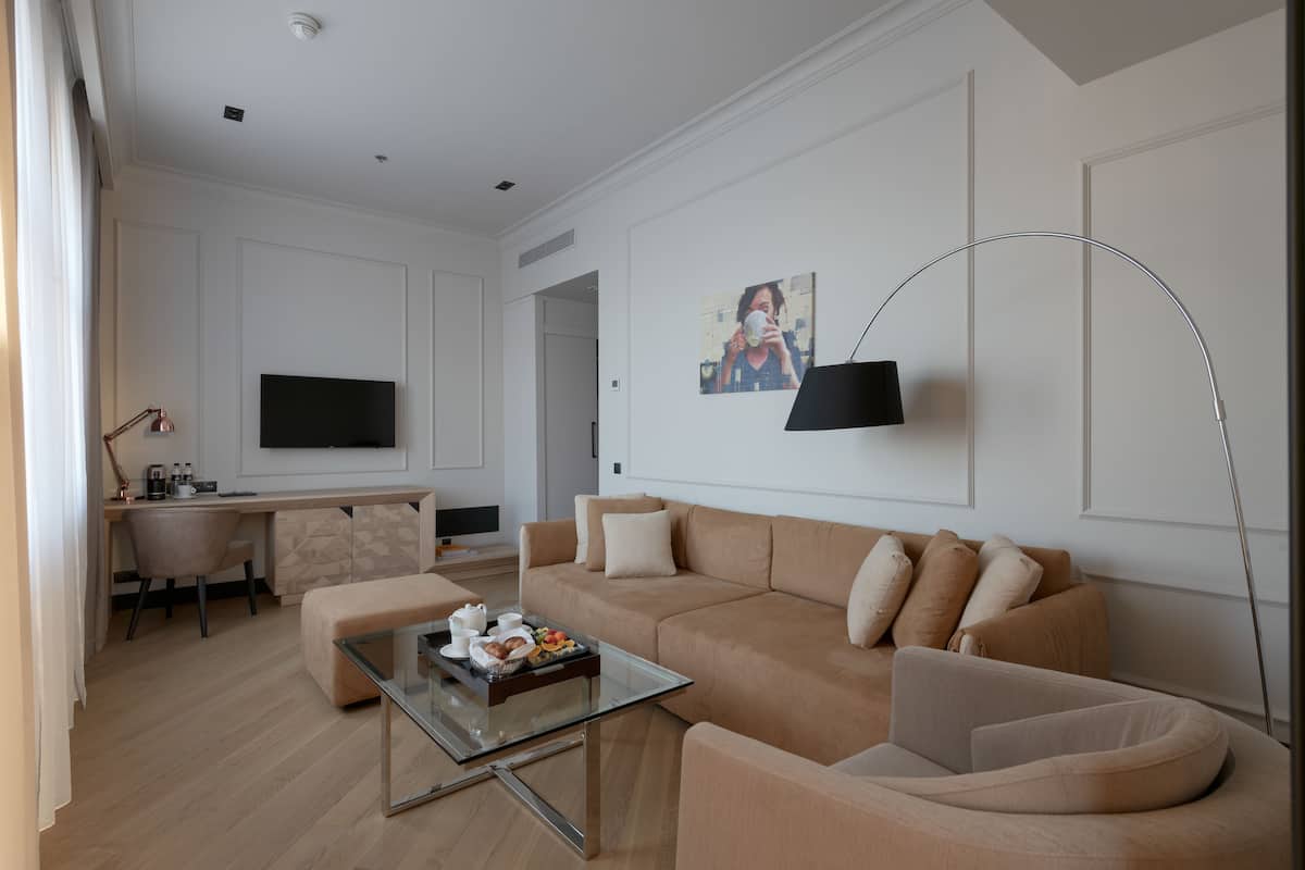 A modern living room with a beige sofa, a glass coffee table, a flat-screen TV, and a painting on the wall.