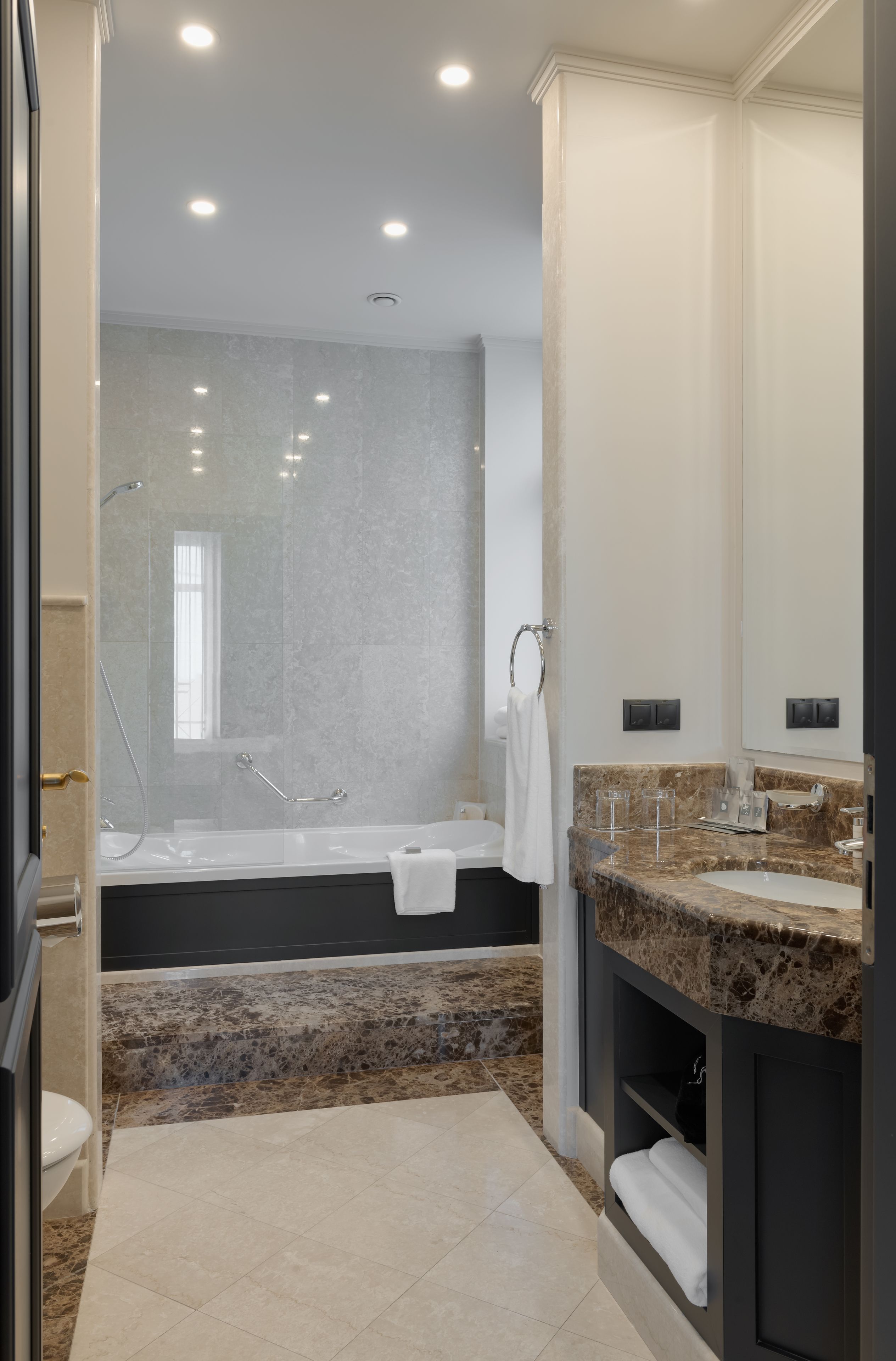 Un baño moderno con bañera, un espejo grande y un lavamanos con encimera de granito.