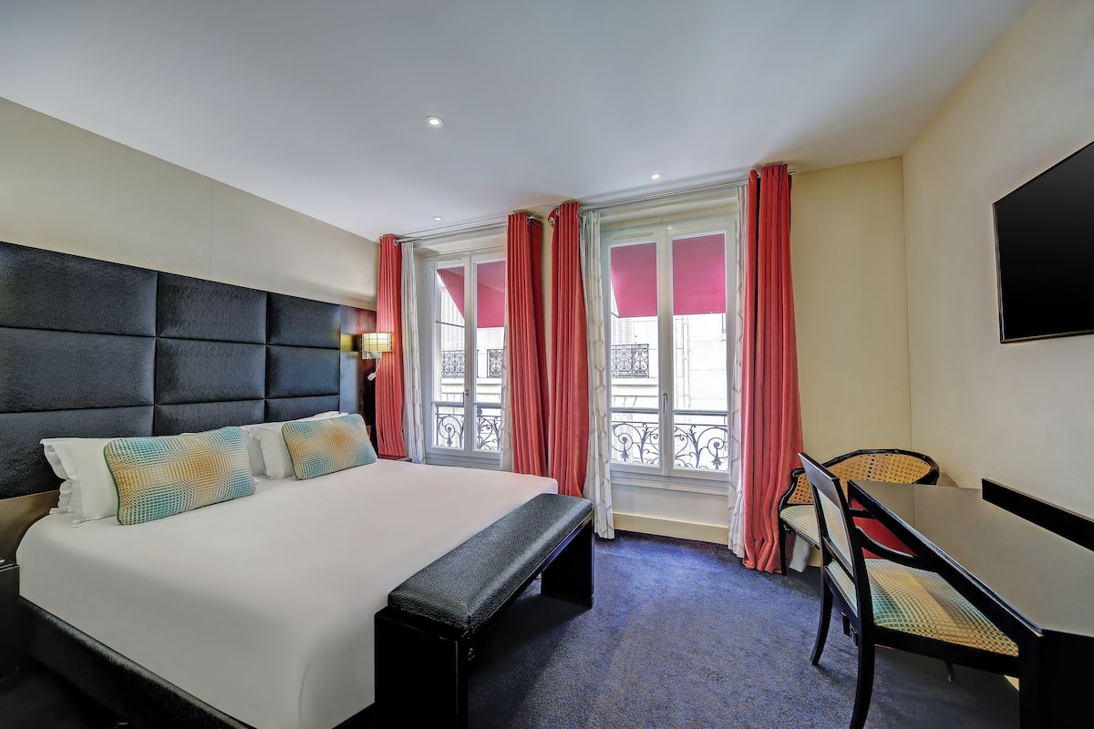A hotel room with a large bed, a desk, and a chair.