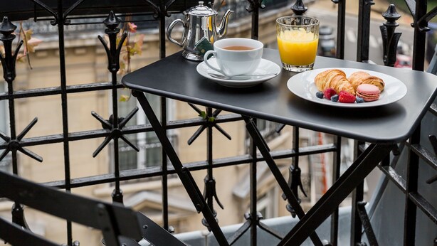 Ein Balkon mit einem Frühstückstisch, einschließlich Croissants, einer Kaffeetasse und einem Glas Orangensaft.