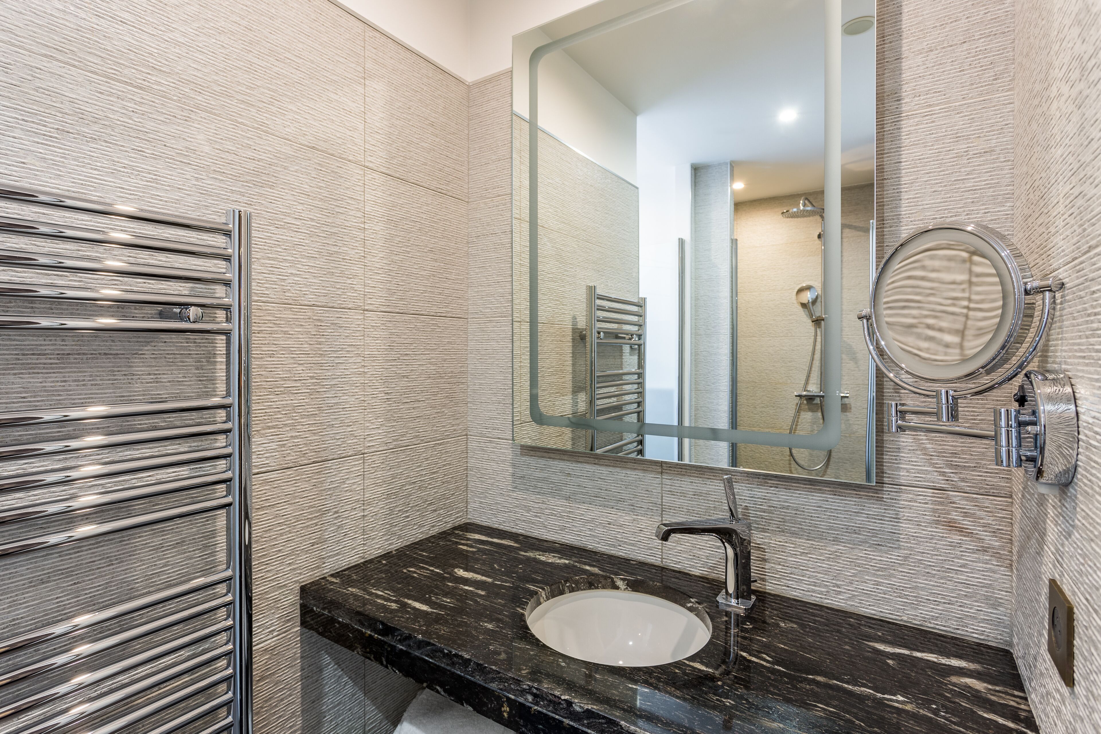 A bathroom with a black marble sink, a chrome towel rack, and a large mirror.