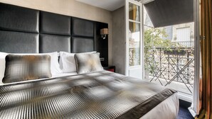 Ein modernes Hotelzimmer mit einem großen Bett, einem dunklen Kopfteil und Blick auf einen Balkon mit schmiedeeisernem Geländer.