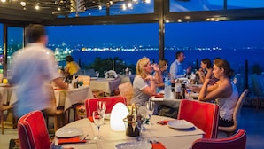 Un restaurante con mesas dispuestas para cenar, sillas y vista panorámica de la ciudad de noche.
